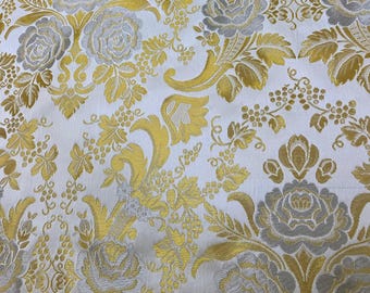 Puede incluir: Tela blanca con un patrón floral dorado y plateado. La tela presenta un diseño repetitivo de rosas y hojas.