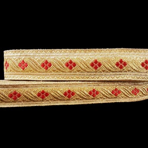 May include: Two rolls of decorative trim with a gold metallic finish and red floral accents. The trim features an intricate woven design, perfect for embellishing garments or craft projects. The background is solid black.