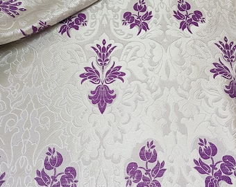 May include: White fabric with a damask pattern featuring purple floral designs. The fabric has a subtle sheen and a textured surface.