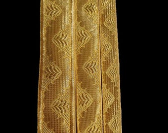 Pode incluir: Três tiras de acabamento decorativo dourado com um padrão de folhas repetido. O acabamento é tecido e tem uma superfície texturizada. As tiras são exibidas verticalmente sobre um fundo preto.