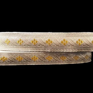 May include: Two rolls of decorative trim with a cream-colored base and gold floral and wave patterns. The trim is likely made of fabric and is suitable for sewing or crafting projects.