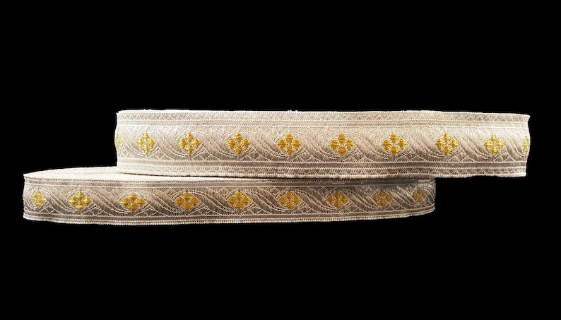 May include: Two rolls of decorative trim with a cream-colored base and gold floral and wave patterns. The trim is likely made of fabric and is suitable for sewing or crafting projects.