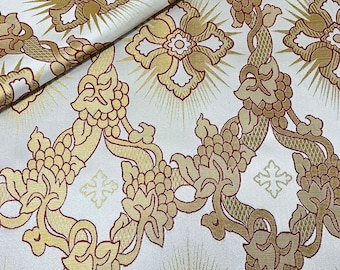 Puede incluir: Tela blanca con un patrón floral dorado y rojo. El patrón presenta un diseño repetitivo de flores estilizadas con una cruz en el centro, rodeadas de vides y uvas.