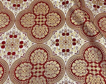 Puede incluir: Tela de brocado roja y dorada con un patrón repetido de cuatrifolios y cruces. La tela tiene un tacto lujoso y texturizado.