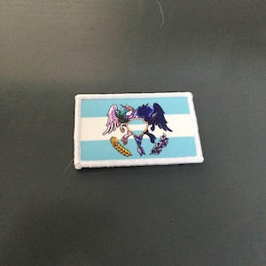 May include: A rectangular patch featuring the flag of Guatemala. The flag has two light blue stripes and a white stripe in the middle. The center of the flag has a colorful emblem with a bird, wings, and other details. The patch is bordered with white stitching.