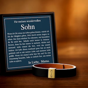 May include: A black leather bracelet with a gold-coloured clasp featuring the infinity symbol, displayed next to a framed message in German. The message is addressed to "Sohn" (Son) from "Mama" (Mum).