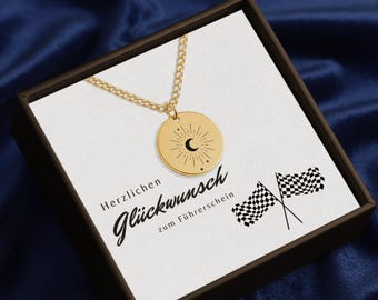 May include: A gold-colored necklace with a round pendant featuring a sun and crescent moon design. The necklace is presented in a gift box with the German text "Herzlichen Glückwunsch zum Führerschein" and checkered flags.