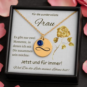 Könnte beinhalten: Goldfarbene Halskette mit rundem Anhänger, blauem Edelstein und Unendlichkeitszeichen. Die Kette wird in einer schwarzen Geschenkbox präsentiert. Der Text auf der Box ist auf Deutsch.