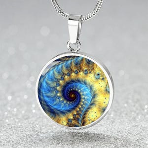 Peut inclure: Un collier en chaîne argent avec un pendentif rond orné d'un motif fractal bleu et jaune.