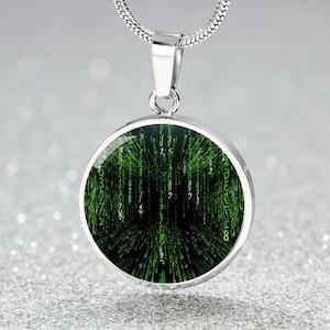 Könnte beinhalten: Eine silberne Halskette mit einem runden Anhänger, der ein grünes und schwarzes digitales Code-Design zeigt. Der Code scheint vom Bildschirm herunterzufallen und erzeugt einen visuellen Effekt von digitalem Regen.