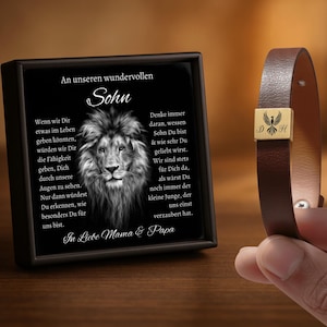 May include: A framed black and white lion portrait with German text, and a brown leather bracelet with a gold-colored clasp. The bracelet clasp has a bird design and the initials "D" and "H".