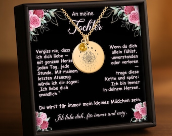 May include: A gold-colored necklace with a round pendant featuring a lotus flower design and a small yellow gemstone. The necklace is displayed in a black box with text in German, including the words "An meine Tochter" and "Ich liebe dich."
