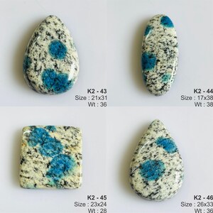 May include: Four K2 stone cabochons with white and black granite-like speckled patterns and vibrant blue circular inclusions. Each piece is labeled with a code, dimensions in mm, and weight in carats: K2-43 (21x31mm, 36ct), K2-44 (17x38mm, 38ct), K2-45 (23x24mm, 28ct), and K2-46 (26x33mm, 36ct).