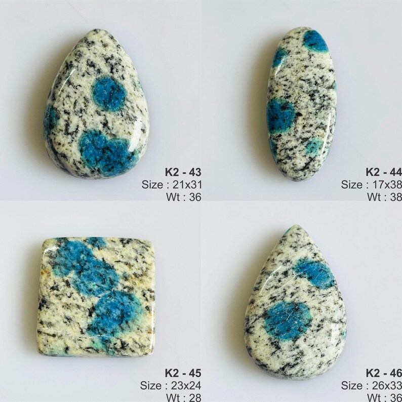 May include: Four K2 stone cabochons with white and black granite-like speckled patterns and vibrant blue circular inclusions. Each piece is labeled with a code, dimensions in mm, and weight in carats: K2-43 (21x31mm, 36ct), K2-44 (17x38mm, 38ct), K2-45 (23x24mm, 28ct), and K2-46 (26x33mm, 36ct).