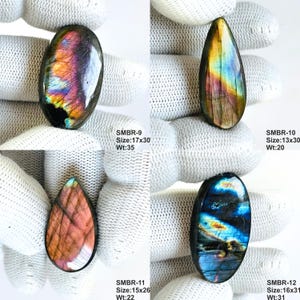 May include: Four polished labradorite gemstones in various shapes. The gemstones display iridescent colors of blue, purple, and gold. Each stone has a unique pattern and is displayed on a white surface. The sizes range from 13x30mm to 17x30mm.