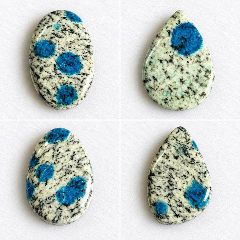 May include: Four polished cabochons featuring a speckled cream and black granite-like matrix with vibrant blue circular inclusions. Two stones are oval-shaped, and two stones are teardrop-shaped, all displaying a smooth, glossy surface finish.