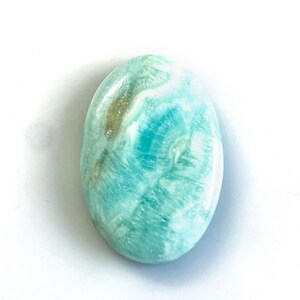 Peut inclure: Une pierre pr&eacute;cieuse polie de forme ovale pr&eacute;sentant un m&eacute;lange vibrant de motifs tourbillonnants turquoise, bleu clair et blancs avec une surface lisse et brillante. La pierre pr&eacute;sente des inclusions min&eacute;rales naturelles.