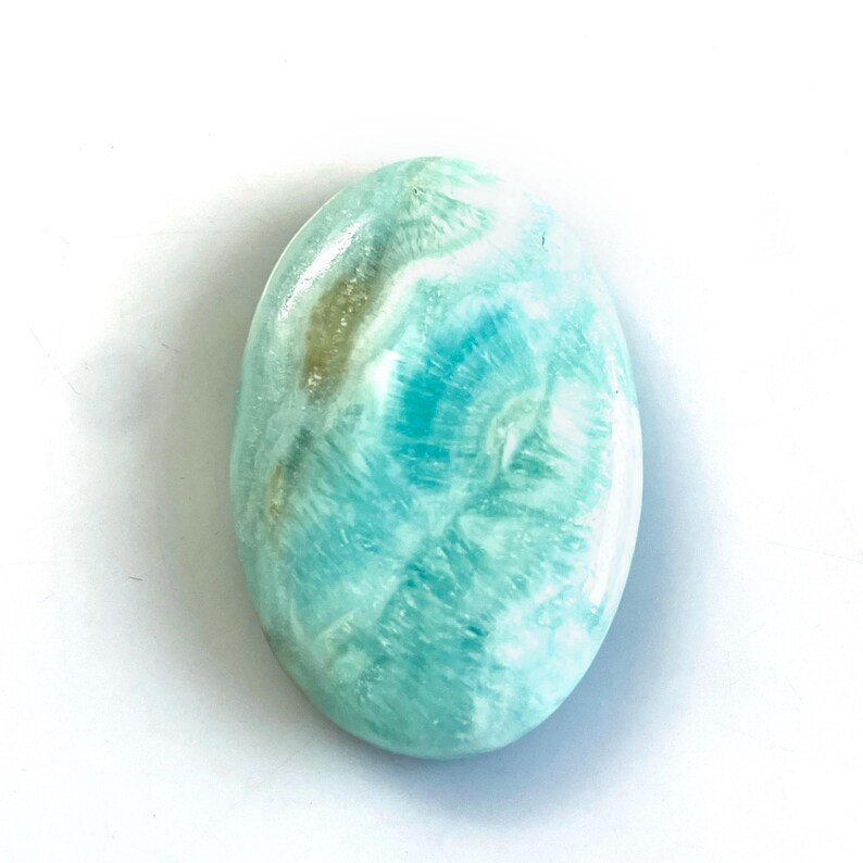 Peut inclure: Une pierre pr&eacute;cieuse polie de forme ovale pr&eacute;sentant un m&eacute;lange vibrant de motifs tourbillonnants turquoise, bleu clair et blancs avec une surface lisse et brillante. La pierre pr&eacute;sente des inclusions min&eacute;rales naturelles.