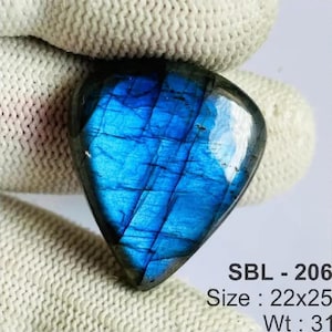 Pode incluir: Uma pedra preciosa de labradorite em forma de lágrima com um brilho azul iridescente vibrante na sua superfície polida. A pedra está marcada com o texto SBL - 206, Size : 22x25, e Wt : 31, indicando a sua identificação e dimensões.