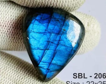 Puede incluir: Una piedra preciosa de labradorita en forma de lágrima con un vibrante destello azul iridiscente en su superficie pulida. La piedra está marcada con el texto SBL - 206, Size : 22x25, y Wt : 31, indicando su identificación y dimensiones.