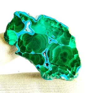 May include: A polished slab of malachite and chrysocolla featuring deep forest green concentric circular patterns contrasted by vibrant, bright turquoise blue veins and inclusions throughout the irregular, organic-shaped mineral specimen.
