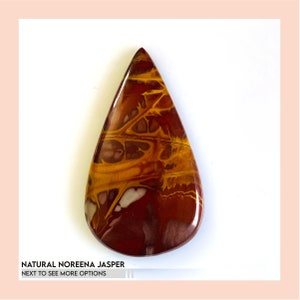 May include: A polished, teardrop-shaped natural Noreena Jasper gemstone. The stone features a mix of deep red, golden yellow, and white patterns. The text "NATURAL NOREENA JASPER" and "NEXT TO SEE MORE OPTIONS" is visible at the bottom.