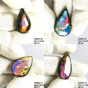 May include: Four teardrop-shaped labradorite gemstones with iridescent colors of blue, purple, and gold. Each stone is held against a white background. The sizes range from 0.43 x 0.87 inches to 0.63 x 0.98 inches.