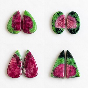 May include: Eight polished zoisite gemstones arranged in four pairs. Each stone features a vibrant magenta-pink center surrounded by a mottled green and black mineral matrix. The shapes include teardrops, ovals, and triangular cabochons.