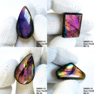 May include: Four polished labradorite gemstones in various shapes. The stones display iridescent colors of purple, pink, and gold. Each stone has a unique shape and size, with the largest measuring 16x26 mm. The image includes the text "SMBR-13", "SMBR-14", "SMBR-15", and "SMBR-16".