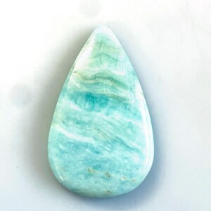 Peut inclure: Une pierre pr&eacute;cieuse polie en forme de goutte d'eau pr&eacute;sentant une surface lisse avec des motifs tourbillonnants de bleu clair, de turquoise et de blanc. La pierre a une finition brillante et pr&eacute;sente des variations de couleur naturelles.