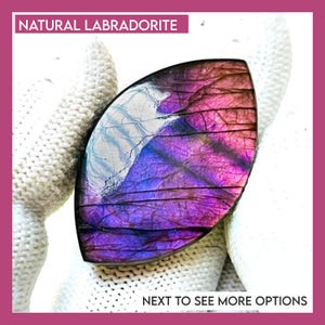 May include: A marquise-shaped natural labradorite gemstone featuring a vibrant purple and blue iridescent flash with visible internal fractures. The stone is labeled with the text NATURAL LABRADORITE and NEXT TO SEE MORE OPTIONS.