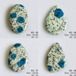 May include: Four polished K2 stone cabochons with white and grey granite-like speckled patterns and vibrant blue circular inclusions. Each piece is labeled with codes K2-35, K2-36, K2-37, and K2-38, including dimensions in mm and weight in carats.