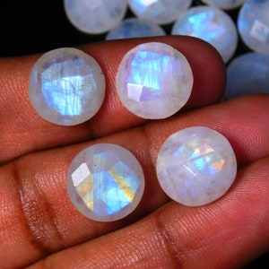May include: Four round, white moonstone cabochons with iridescent blue and gold flashes. The stones are faceted and have a smooth, polished finish.