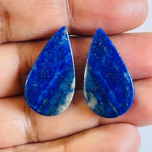 May include: Pair of teardrop-shaped lapis lazuli cabochons with a blue and white marbled pattern. The stones are approximately 2.5 cm long and 1.5 cm wide.