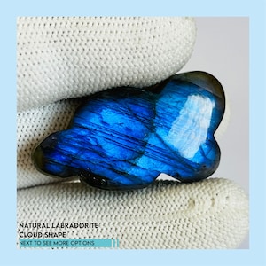 May include: A natural labradorite gemstone carved in a cloud shape. The stone features a vibrant blue color with streaks of darker blue and black. The text on the image reads "NATURAL LABRADORITE CLOUD SHAPE NEXT TO SEE MORE OPTIONS."