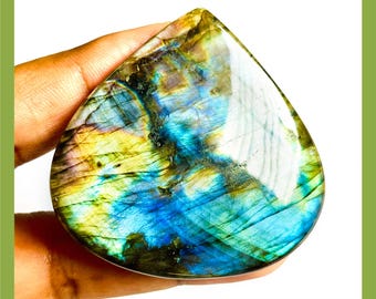 Peut inclure: Une pierre précieuse de labradorite naturelle polie en forme de goutte, présentant des reflets irisés bleus, dorés et verts. Le texte "NATURAL LABRADORITE" figure en haut et "NEXT TO SEE MORE OPTIONS" est inscrit en bas.