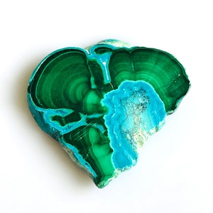 May include: A polished, heart-shaped gemstone with a striking combination of colors. The stone features swirling patterns of deep green and vibrant turquoise, creating a unique and natural design. The gemstone is set against a white background.