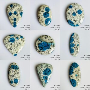 May include: A collection of nine polished K2 granite cabochons featuring a speckled white and grey base with distinct circular blue azurite inclusions. Each stone is labeled with a reference code, dimensions in millimeters, and weight in carats.