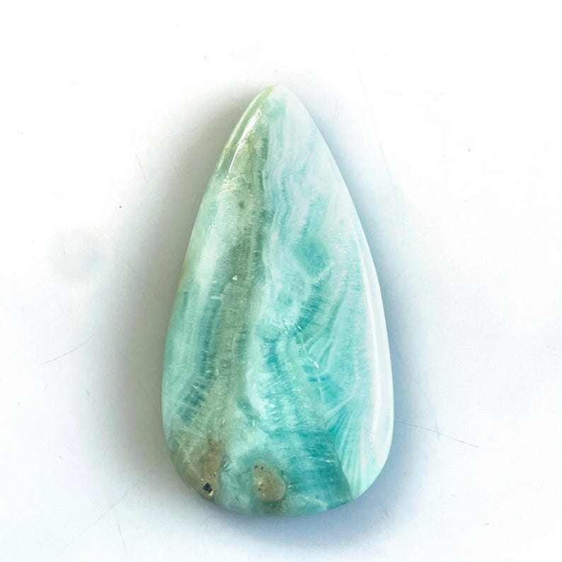 Peut inclure: Une pierre pr&eacute;cieuse cabochon polie en forme de goutte, pr&eacute;sentant une surface lisse avec des motifs tourbillonnants bleu clair, turquoise et blanc, agr&eacute;ment&eacute;e de subtiles inclusions brun gris&acirc;tre pr&egrave;s de la base arrondie.