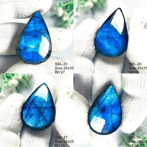 Pu&ograve; includere: Quattro pietre preziose di labradorite a forma di goccia con riflessi blu iridescenti e venature scure. Ogni pietra &egrave; etichettata con i codici SBL-25, SBL-26, SBL-27 e SBL-28, incluse dimensioni in mm e peso in carati, come 20x30 mm e 27 ct.