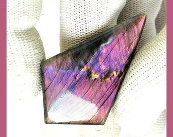 May include: A natural labradorite gemstone with a vibrant display of purple, pink, and iridescent colors. The stone is cut into a unique shape and features the text "NATURAL LABRADORITE" and "NEXT TO SEE MORE OPTIONS".