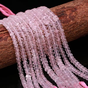 Peut inclure: Gros plan sur plusieurs brins de perles de quartz rose rose clair. Les perles sont facettées et enfilées sur un fil rose. Les perles sont présentées sur un fond sombre. L'effet général est délicat et féminin. Les perles sont de taille et de forme uniformes.