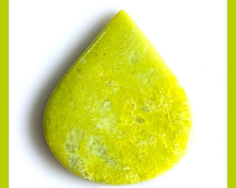 Peut inclure: Un cabochon en forme de goutte d'eau en serpentine verte naturelle avec une surface lisse et polie. La pierre présente une couleur vert citron vibrante avec des textures cristallines marbrées. Le texte NATURAL GREEN SERPENTINE est visible.