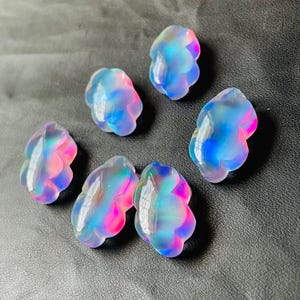 May include: Six iridescent resin cloud-shaped charms in shades of blue, pink, and white. The charms are translucent and have a shimmery finish.