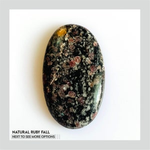 Peut inclure: Une pierre précieuse ovale noire en cabochon avec des reflets rouges et dorés. La pierre est polie et a une surface lisse.