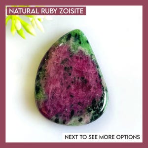 May include: A natural ruby zoisite gemstone with a teardrop shape. The stone features a vibrant mix of colors, including deep magenta, green, and black speckles. The text "NATURAL RUBY ZOISITE" is at the top, and "NEXT TO SEE MORE OPTIONS" is at the bottom.