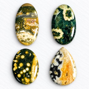 Op de afbeelding: Vier gepolijste cabochons met opvallende natuurlijke patronen. Twee zijn ovaalvormig met groene, gele en witte orbiculaire insluitingen. Eén is een donkergroen ovaal met witte bloemachtige patronen. Eén is druppelvormig met zwarte, witte en gele wervelingen.