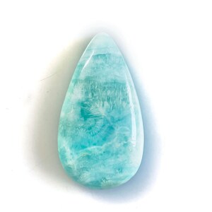 Peut inclure: Une pierre pr&eacute;cieuse larimar polie en forme de goutte, pr&eacute;sentant une surface lisse et brillante avec des motifs tourbillonnants bleu ciel, turquoise et blanc. La pierre affiche une texture marbr&eacute;e aux nuances de bleu et de blanc.
