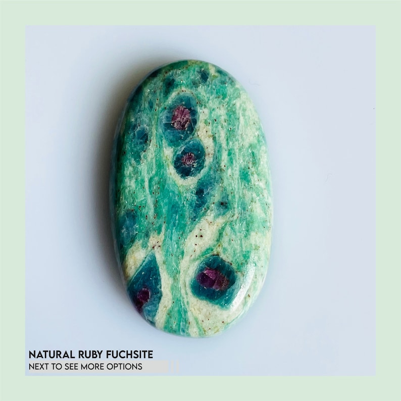 May include: An oval-shaped polished ruby fuchsite gemstone featuring a marbled pattern of vibrant green and creamy white tones with embedded deep magenta-coloured ruby inclusions. The text NATURAL RUBY FUCHSITE NEXT TO SEE MORE OPTIONS is visible.