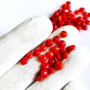 May include: A collection of small, round, vibrant red cabochons with a smooth, polished finish. These circular beads feature a consistent bright red hue and a domed top surface, suitable for jewelry making and various decorative craft projects.